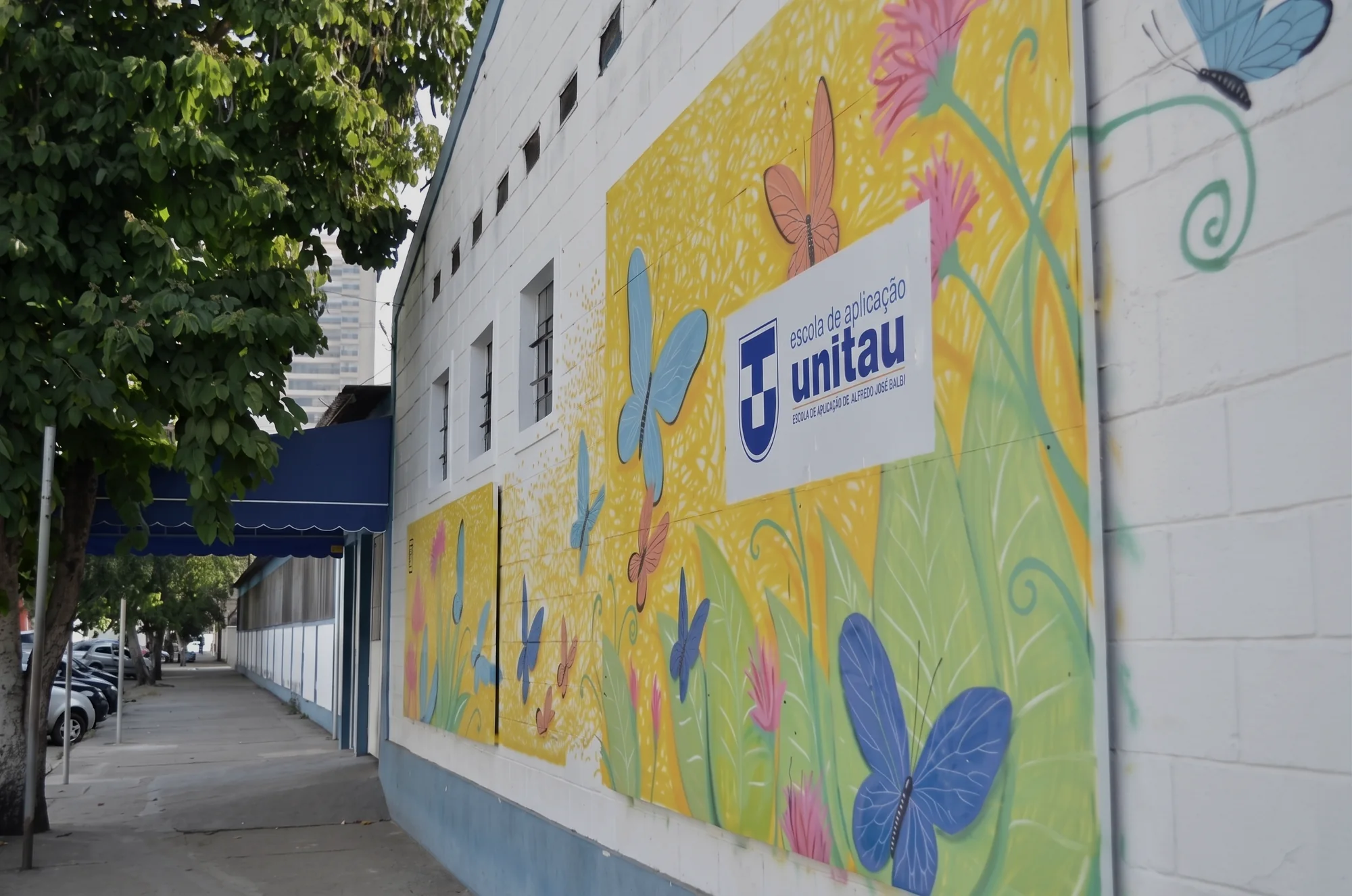Muro pintado com borboletas e a placa da Escola de Aplicação UNITAU